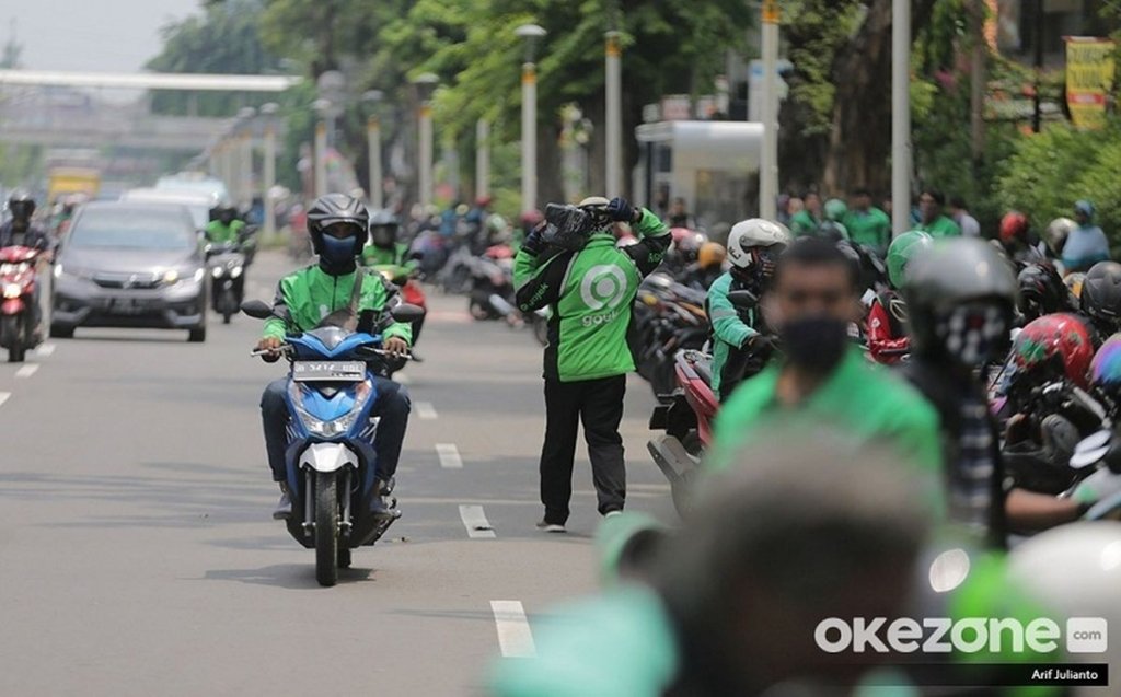 aturan ojol dan aplikator - Ilustrasi pengemudi ojek online (ojol) saat melintas di jalan raya perkotaan.
